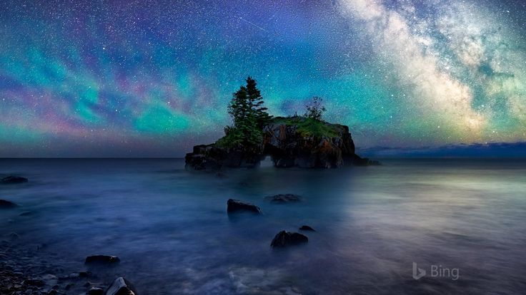 the night sky is filled with stars and aurora lights over an island in the ocean