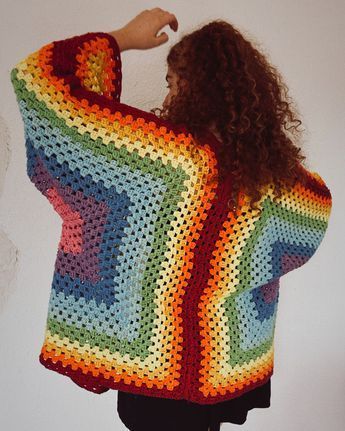 a woman wearing a multicolored crocheted granny shawl with her arms behind her back