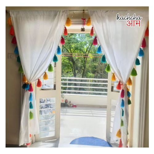 an open window with white curtains and colorful tassels hanging from the windowsill