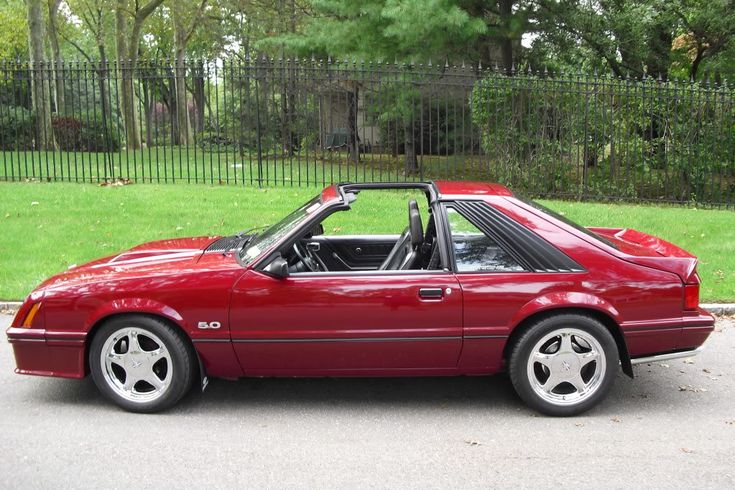 a red sports car parked in front of a fenced area with green grass and trees