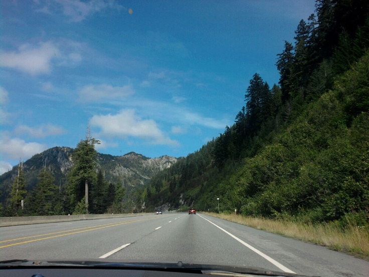 a car driving down the road with mountains in the background and trees on both sides