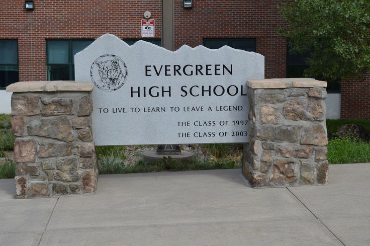 a sign for evergreen high school in front of a brick building with grass and trees