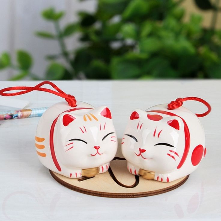 two ceramic cats sitting on top of a wooden stand with a red ribbon around its neck