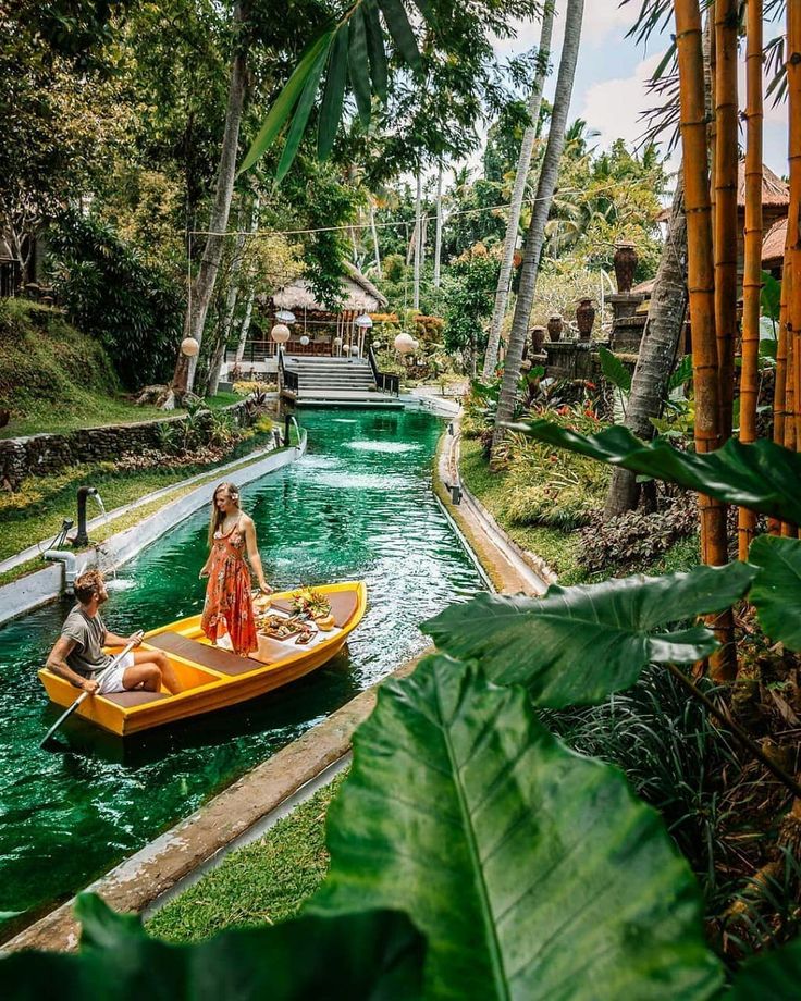 a man and woman in a yellow boat floating down a river surrounded by palm trees