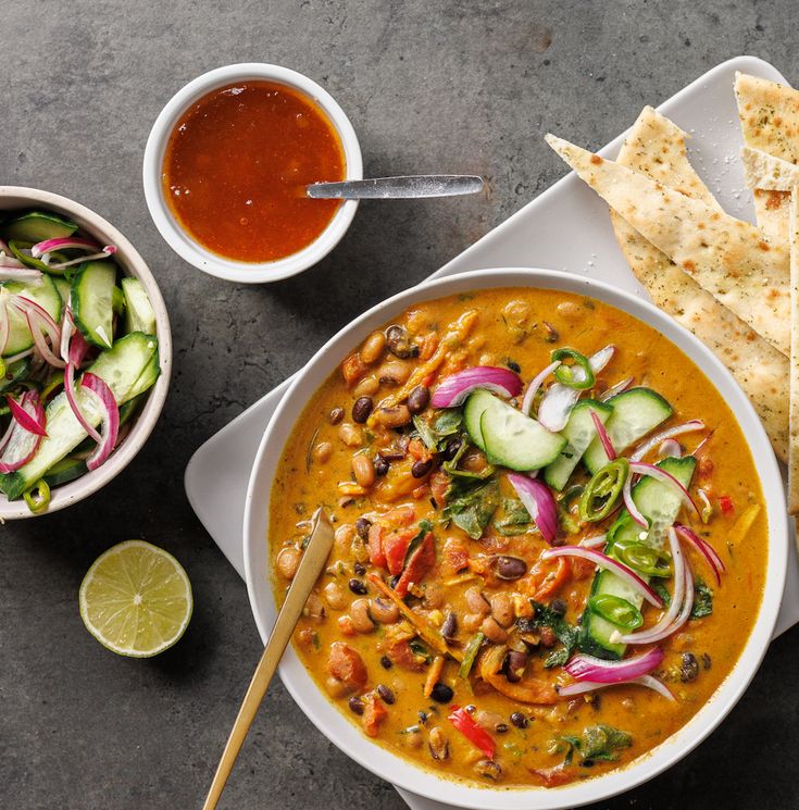 a bowl of soup with tortilla chips, cucumber and sauce on the side