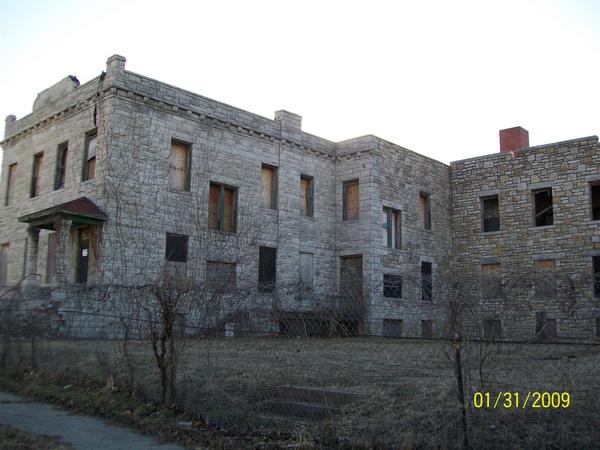 an old brick building with lots of windows and bars on the side of it in front of a chain link fence