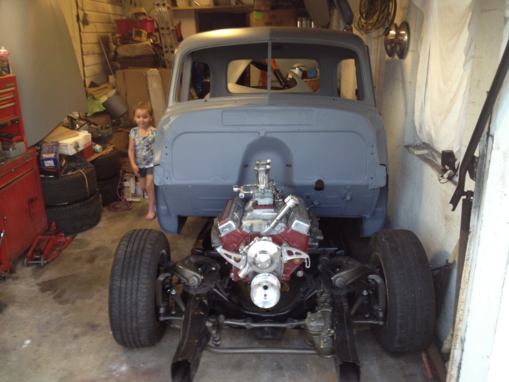 a small child standing next to an old car in a garage