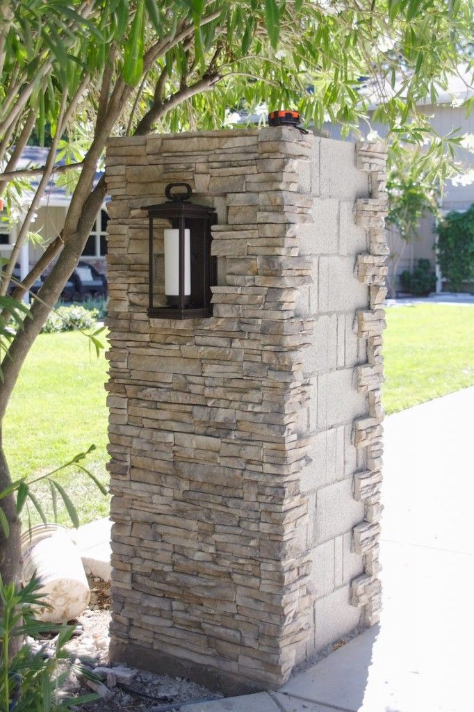 a stone wall with a lantern on it in front of a tree and grass area