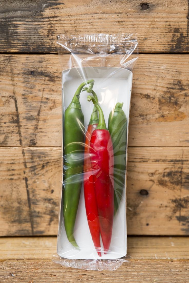 two red and green peppers sitting in a plastic bag on top of a wooden table