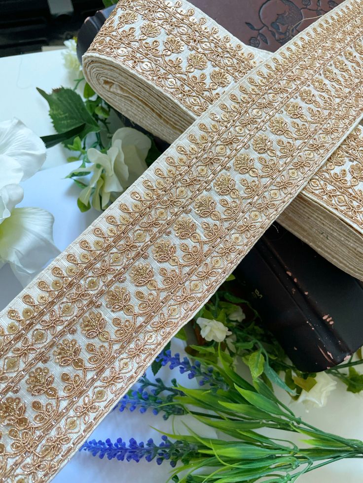 a pair of gold sequins on white ribbon with flowers in the back ground