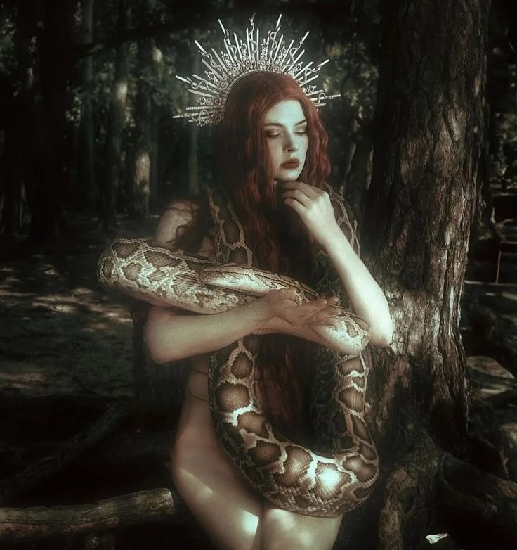 a woman with a crown on her head is holding a snake in the middle of a forest