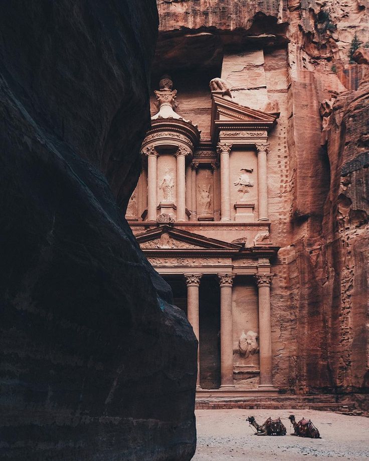 some people are standing in front of an old building that is carved into the side of a mountain