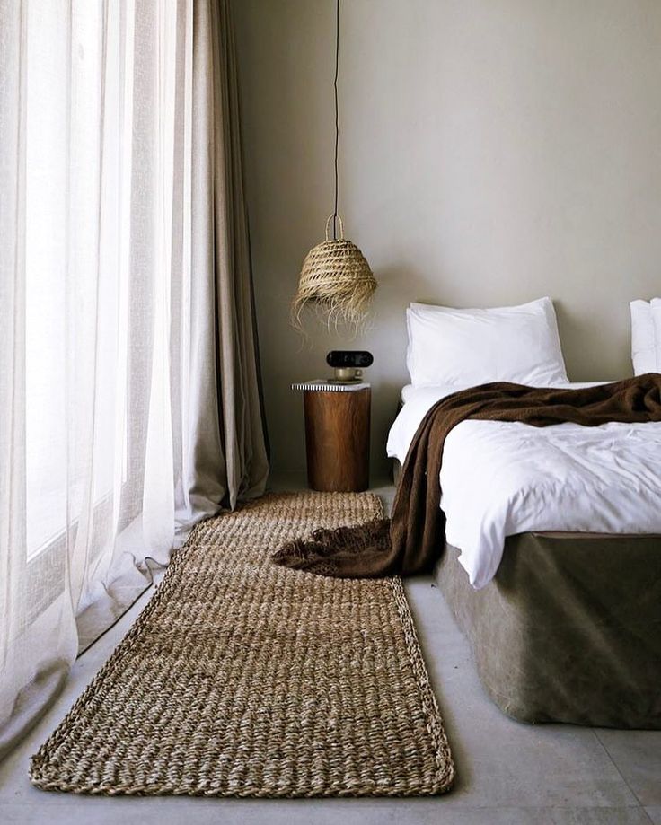 a bed room with a neatly made bed next to a window and a rug on the floor