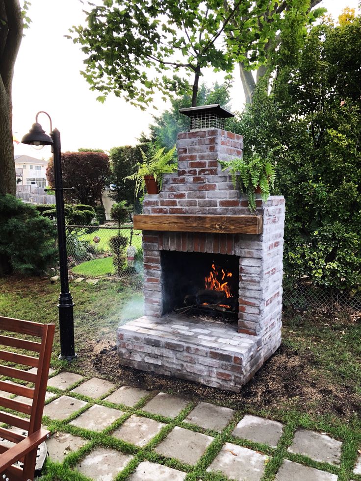 an outdoor brick fireplace with potted plants on top and fire in the middle, surrounded by stone pavers