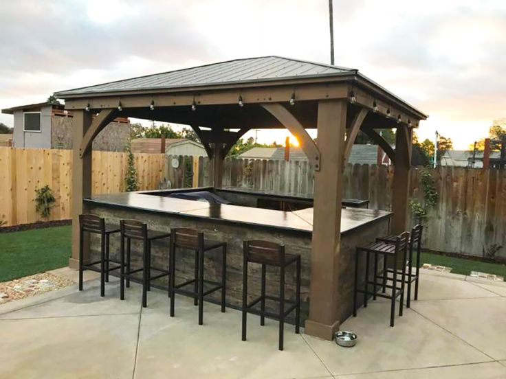 an outdoor bar with stools and tables in the middle of a backyard area at sunset