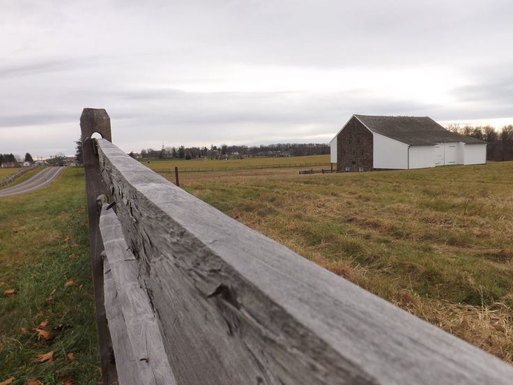 an old wooden fence in front of a farm with a barn and road behind it