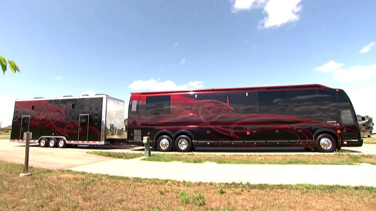 a black and red tour bus parked on the side of the road next to a palm tree