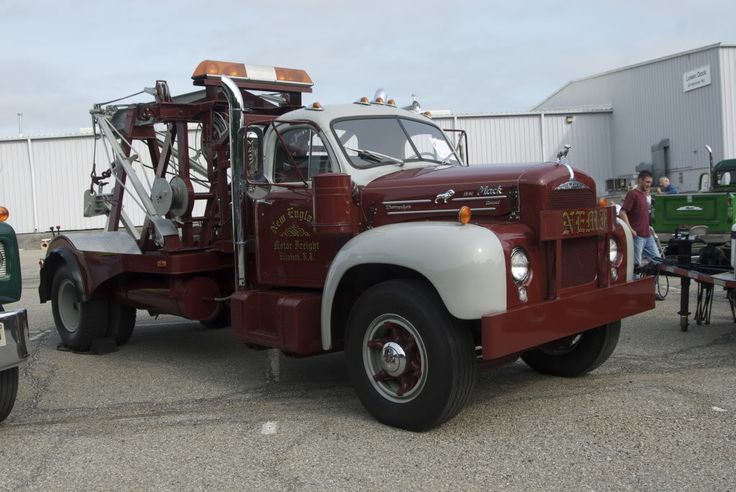 an old red fire truck parked in front of a building with people standing around it