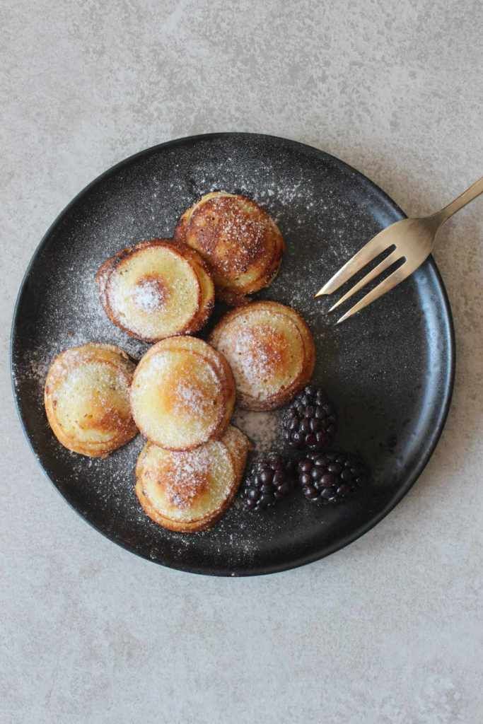 a black plate topped with powdered donuts and berries next to a knife and fork