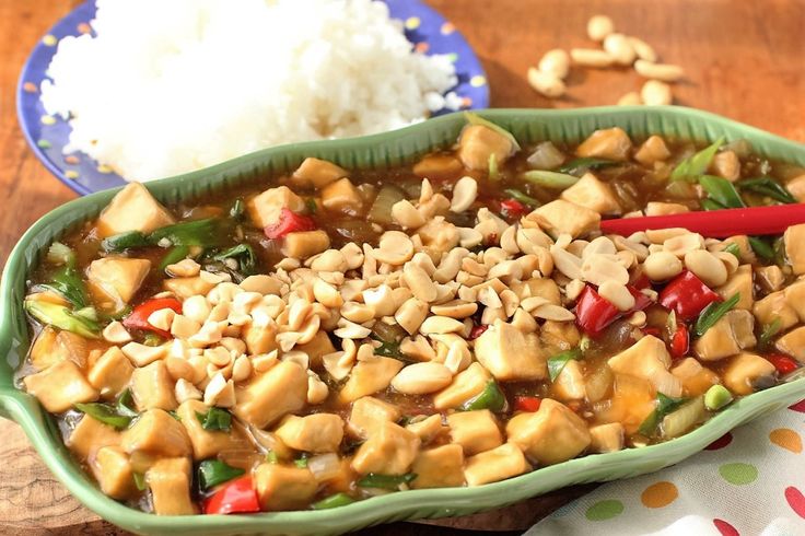 a green bowl filled with food next to rice on top of a wooden tablecloth