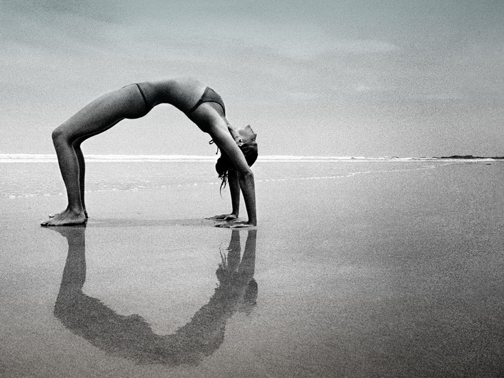 a woman doing yoga on the beach with her hands behind her head and legs bent forward