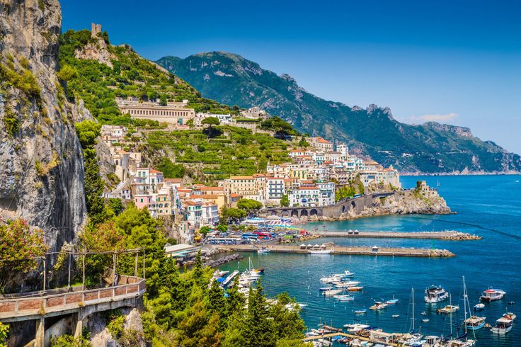 boats are docked in the water next to a mountain side town with cliffs on both sides