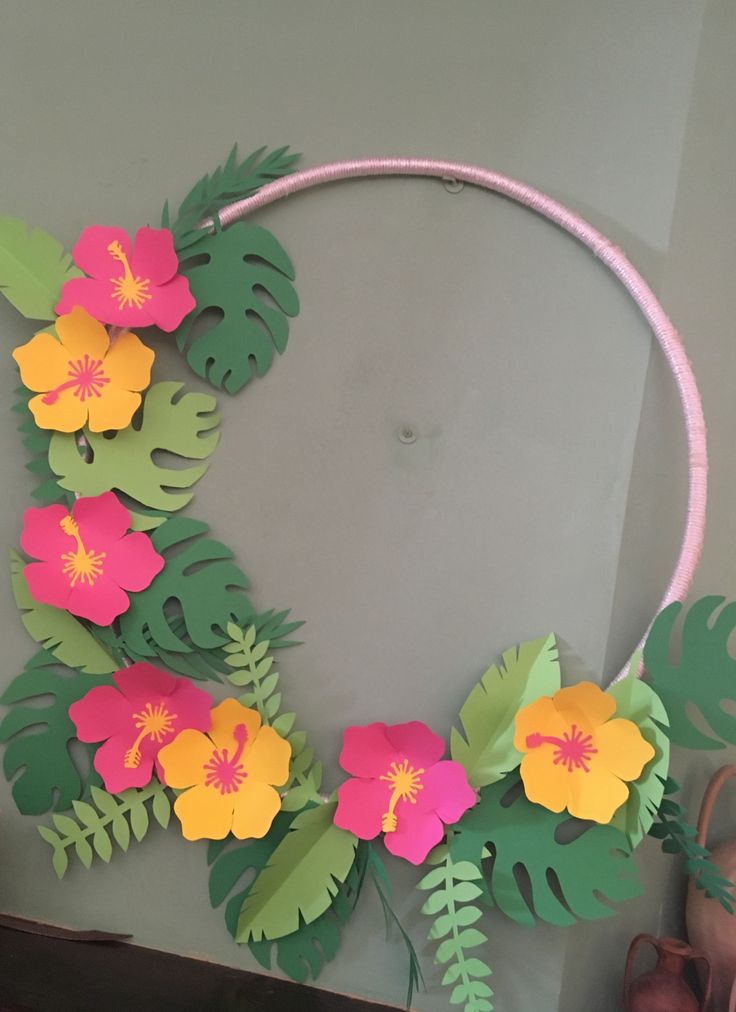 a wreath made out of paper with flowers and leaves on the front, hanging from a wall