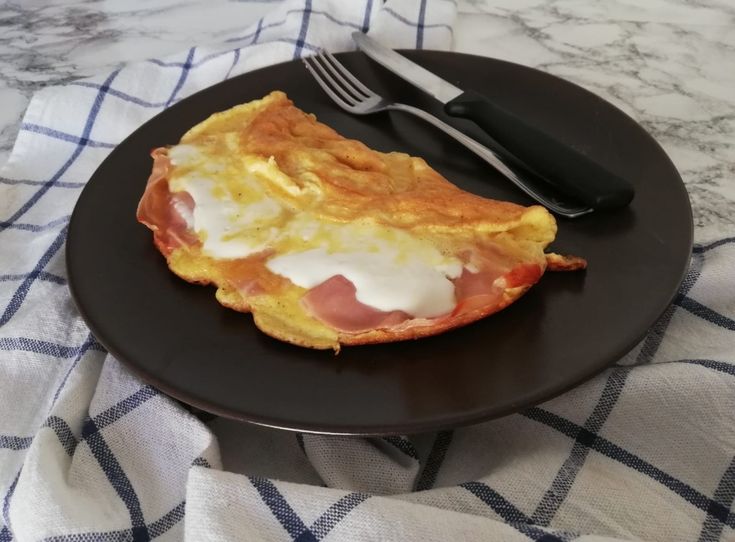 a black plate topped with an omelet covered in cheese and bacon next to a fork