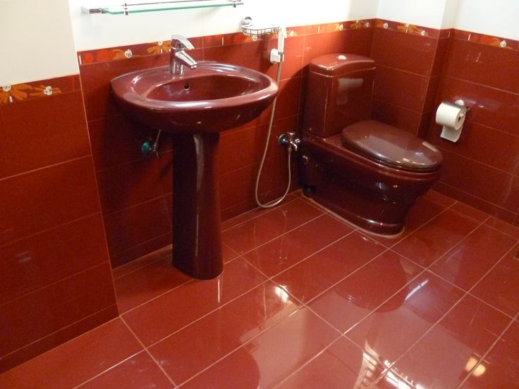 a toilet and sink in a bathroom with red tiles on the floor, walls and floors