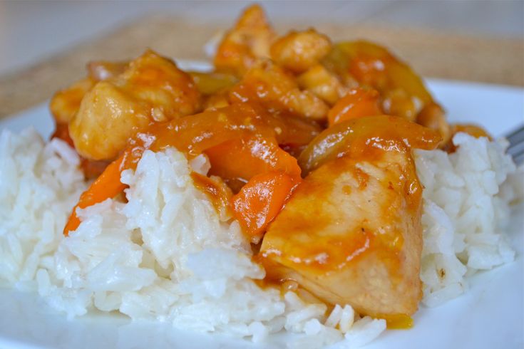 a white plate topped with rice covered in chicken and orange sauce next to a fork