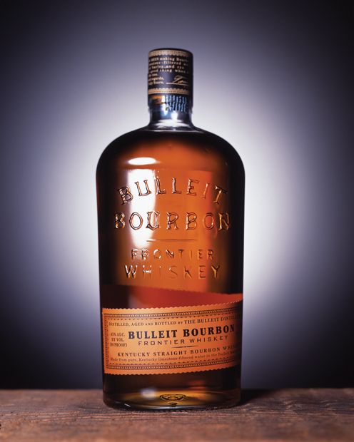 a bottle of whiskey sitting on top of a wooden table next to a black and white background