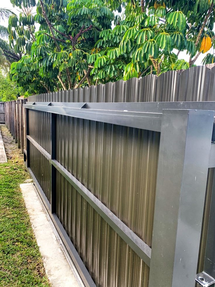 a metal fence in front of a tree and grass area with trees on either side