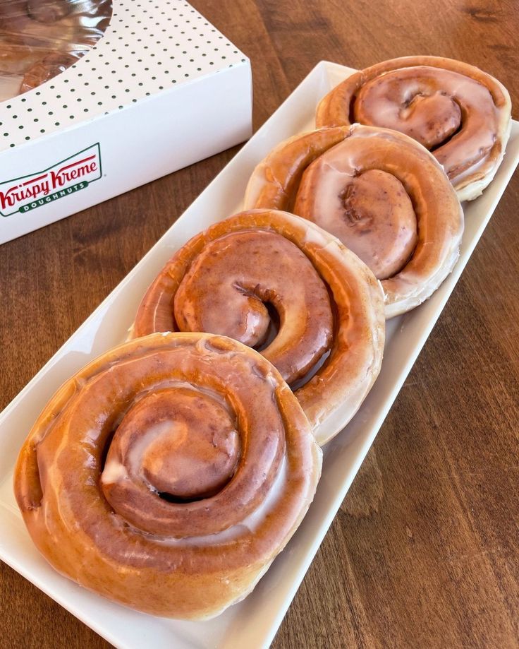 four glazed donuts on a white plate next to a box of doughnuts