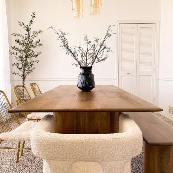 a vase with flowers on top of a wooden table in a room filled with chairs