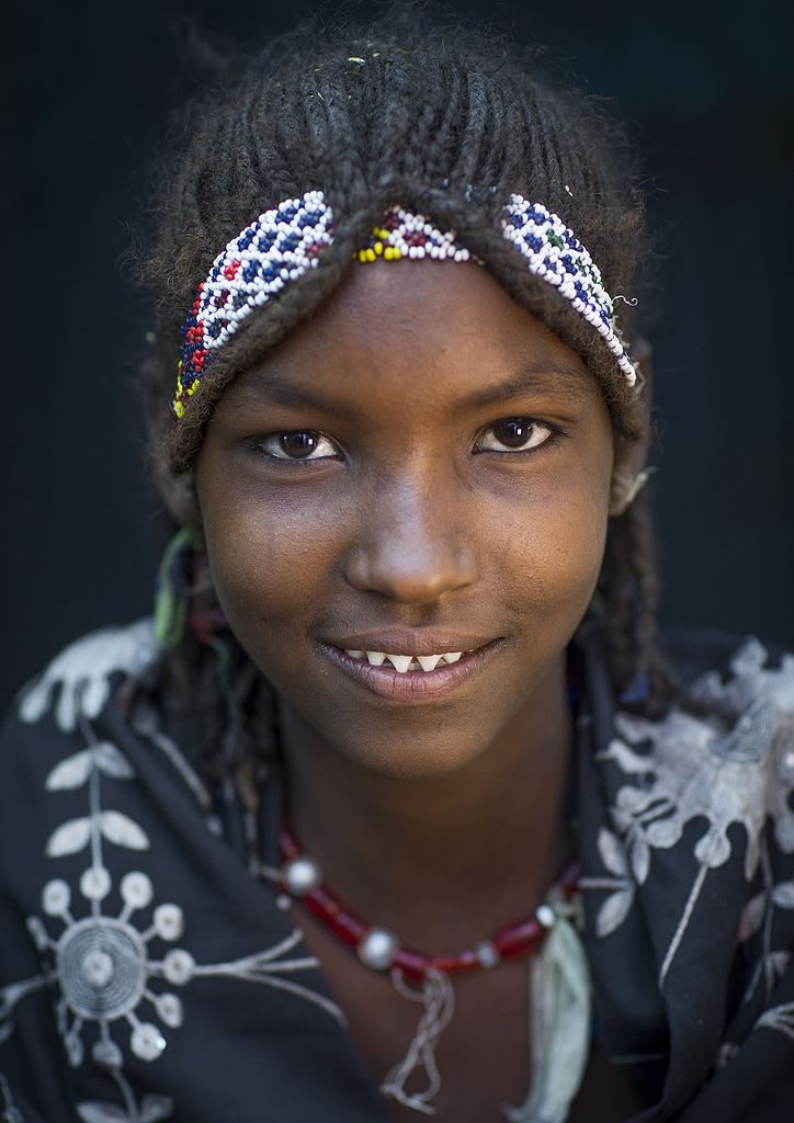 a smiling woman with braids and beads on her head is looking at the camera