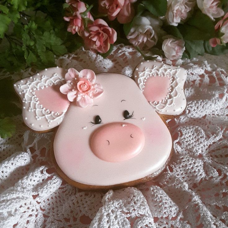 a pink pig cookie sitting on top of a lace covered tablecloth next to flowers