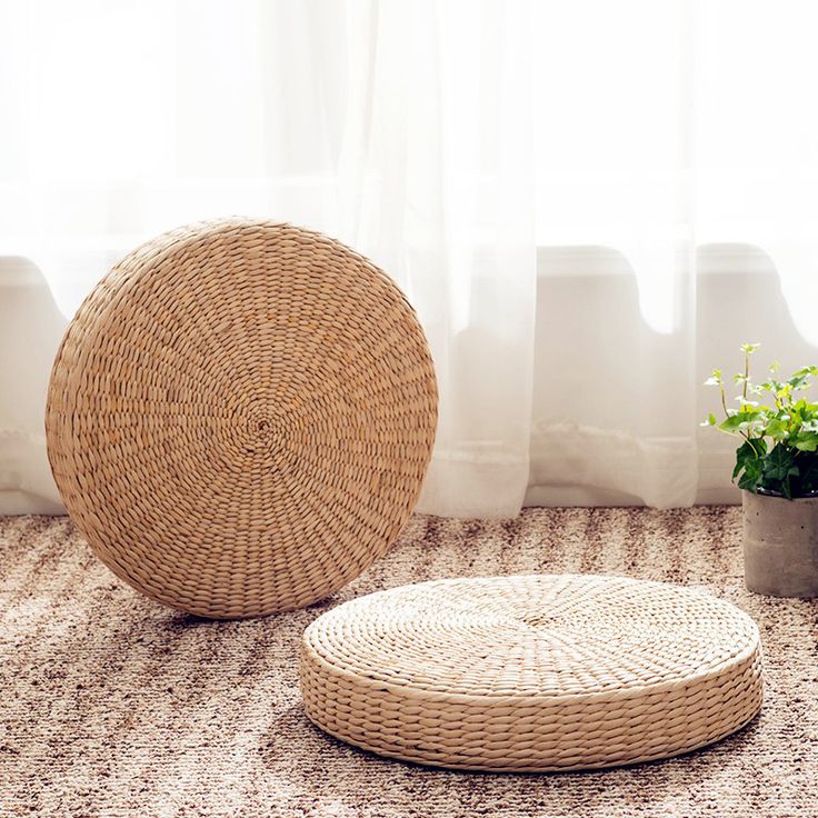 a round wicker ottoman sitting on top of a rug next to a potted plant