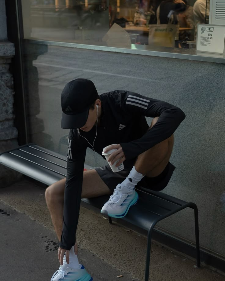 a man is sitting on a bench with his headphones in his ears and drinking from a water bottle