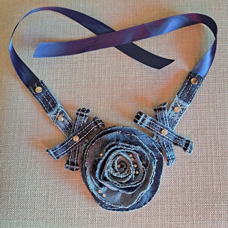 a piece of clothing with a flower on it is hanging from a blue ribbon that has been made into a necklace