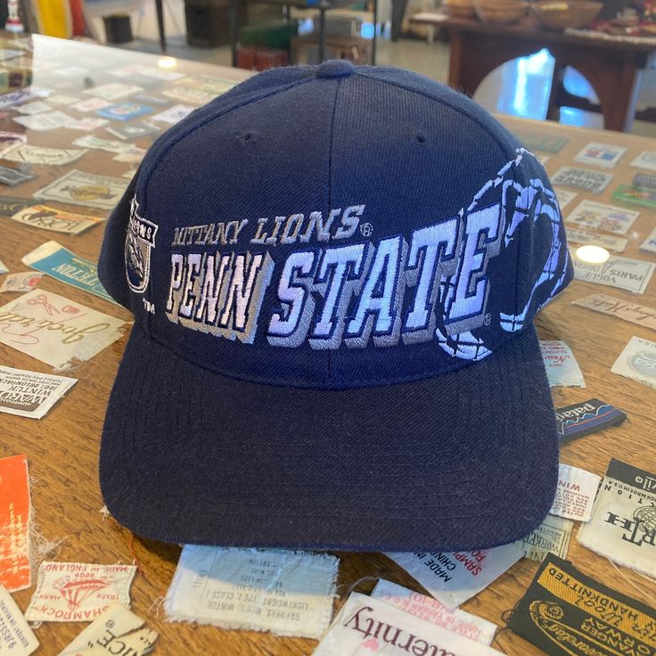 the penn state hat is sitting on top of a table covered with pins and stickers