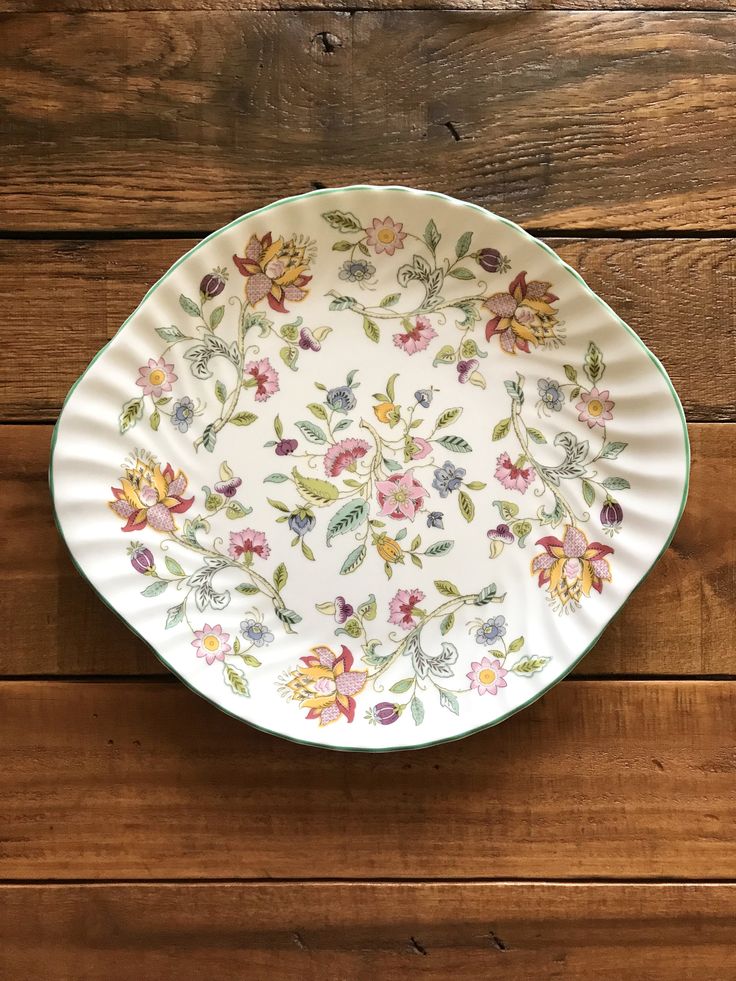 a white plate with flowers on it sitting on top of a wooden table next to a wall