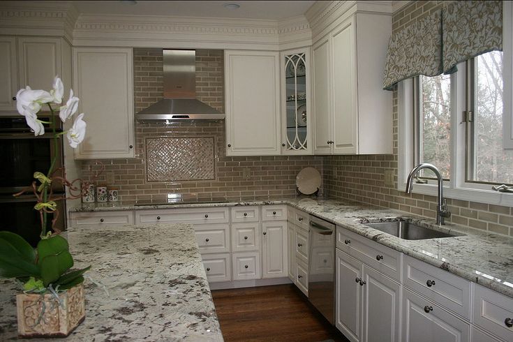 a kitchen with marble counter tops and white cabinets, along with a vase filled with flowers