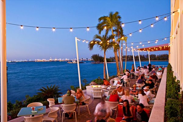 people sitting at tables near the water with string lights strung over them and palm trees