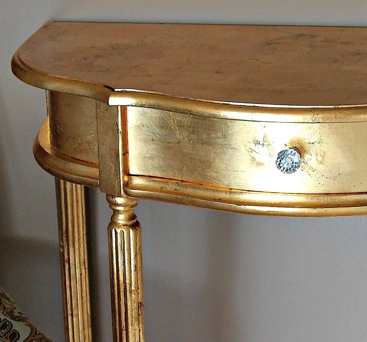 a gold console table with a blue knob on it's drawer and two legs