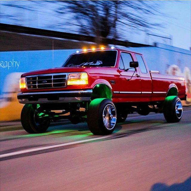 a red truck driving down a street next to a tall building with lights on it