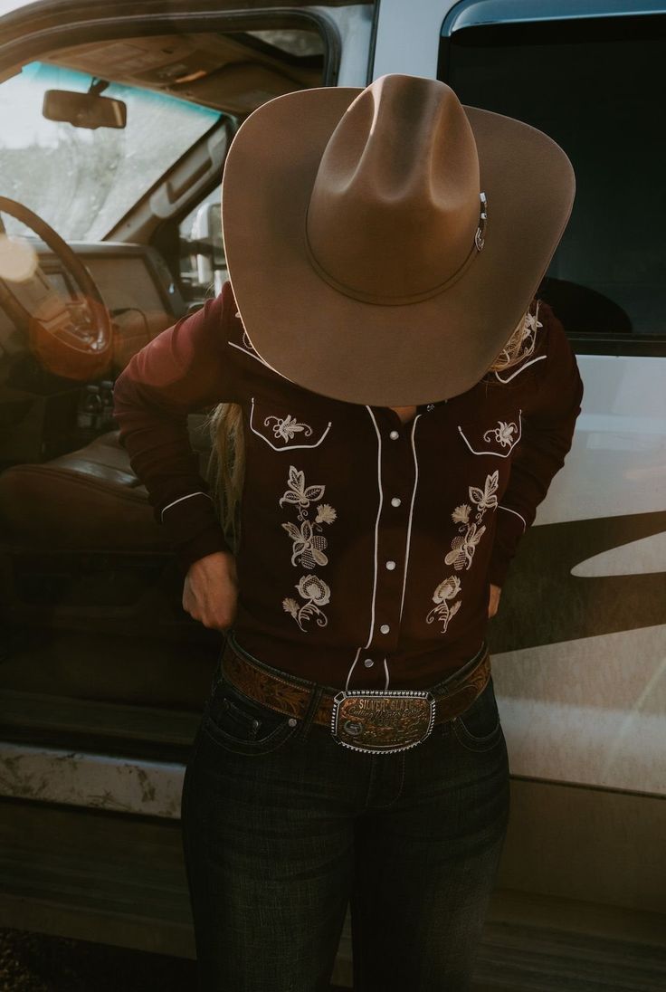 a woman wearing a cowboy hat standing next to a car