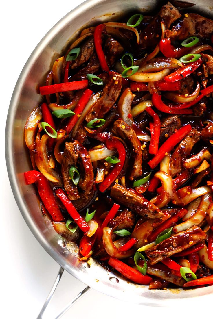 a pan filled with meat and peppers on top of a white countertop next to utensils