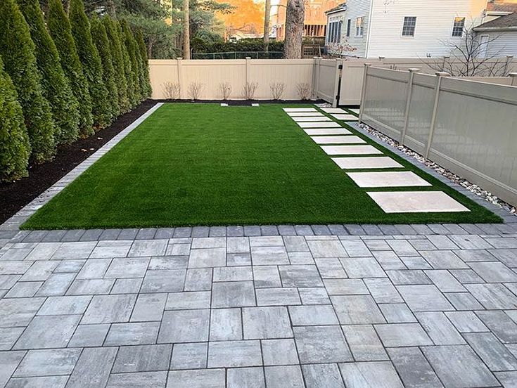 a backyard with grass and white stepping stones on the ground in front of a fence