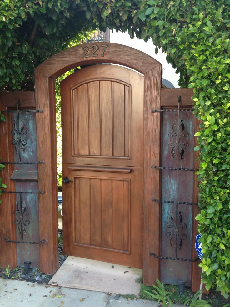 an open wooden door in the middle of a garden with ivy growing on it's sides