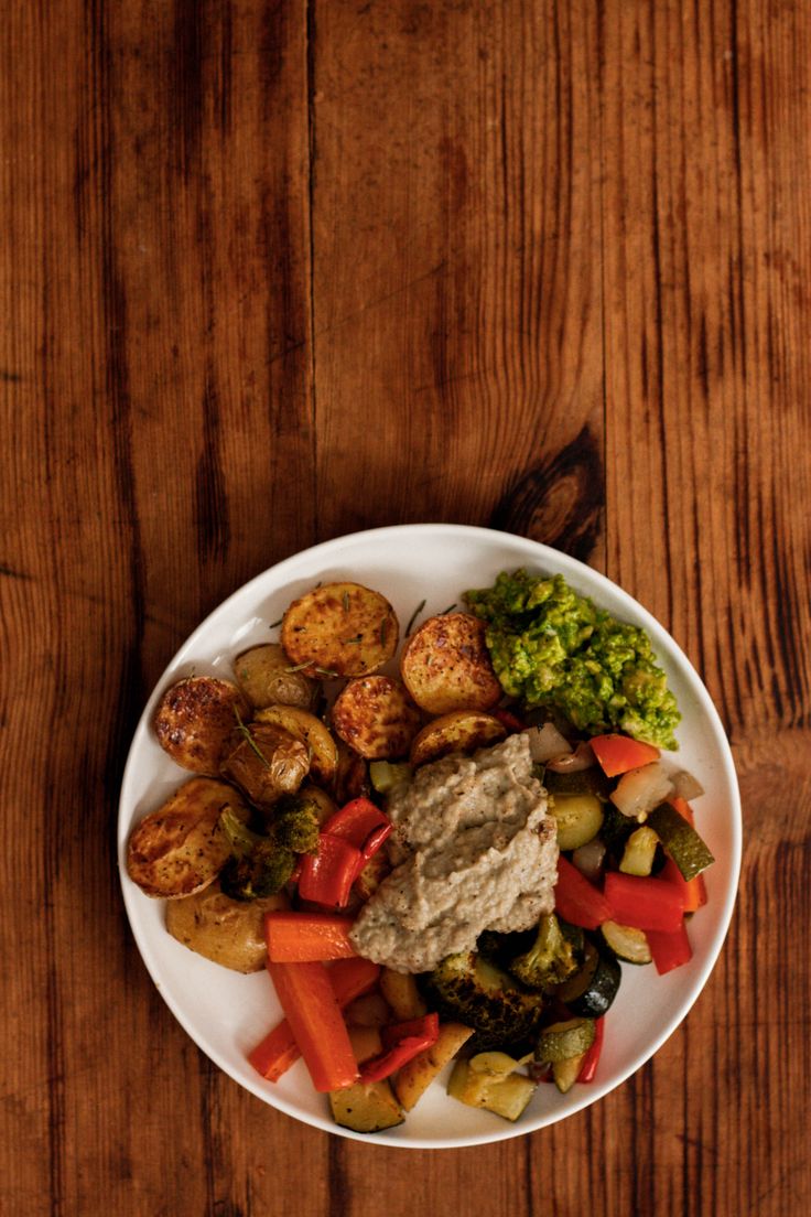 a white plate topped with potatoes and veggies on top of a wooden table